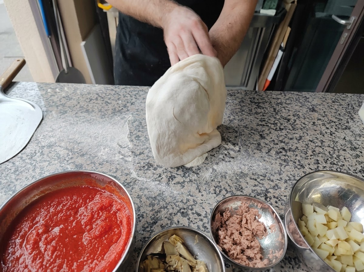 Eine Person dehnt Pizzateig über ihre Fäuste in der Luft.