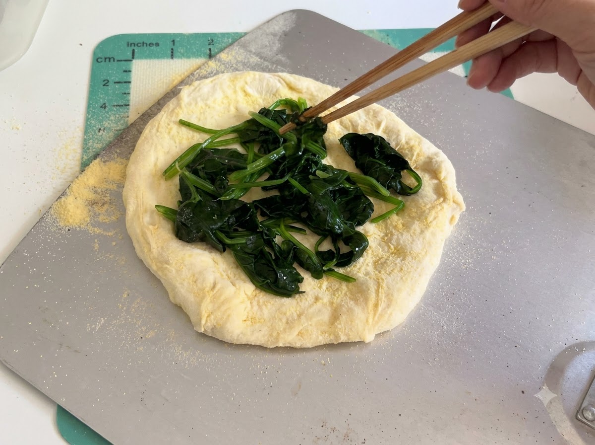 Scheiben weißen Käses werden sorgfältig mit Essstäbchen auf der SpinatSchicht des rohen Pizzateigs angeordnet.