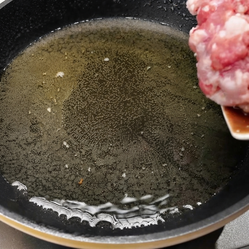 Gehacktes Schweinefleisch wird in eine heiße Pfanne mit Öl gegeben, um den Kochvorgang zu beginnen.