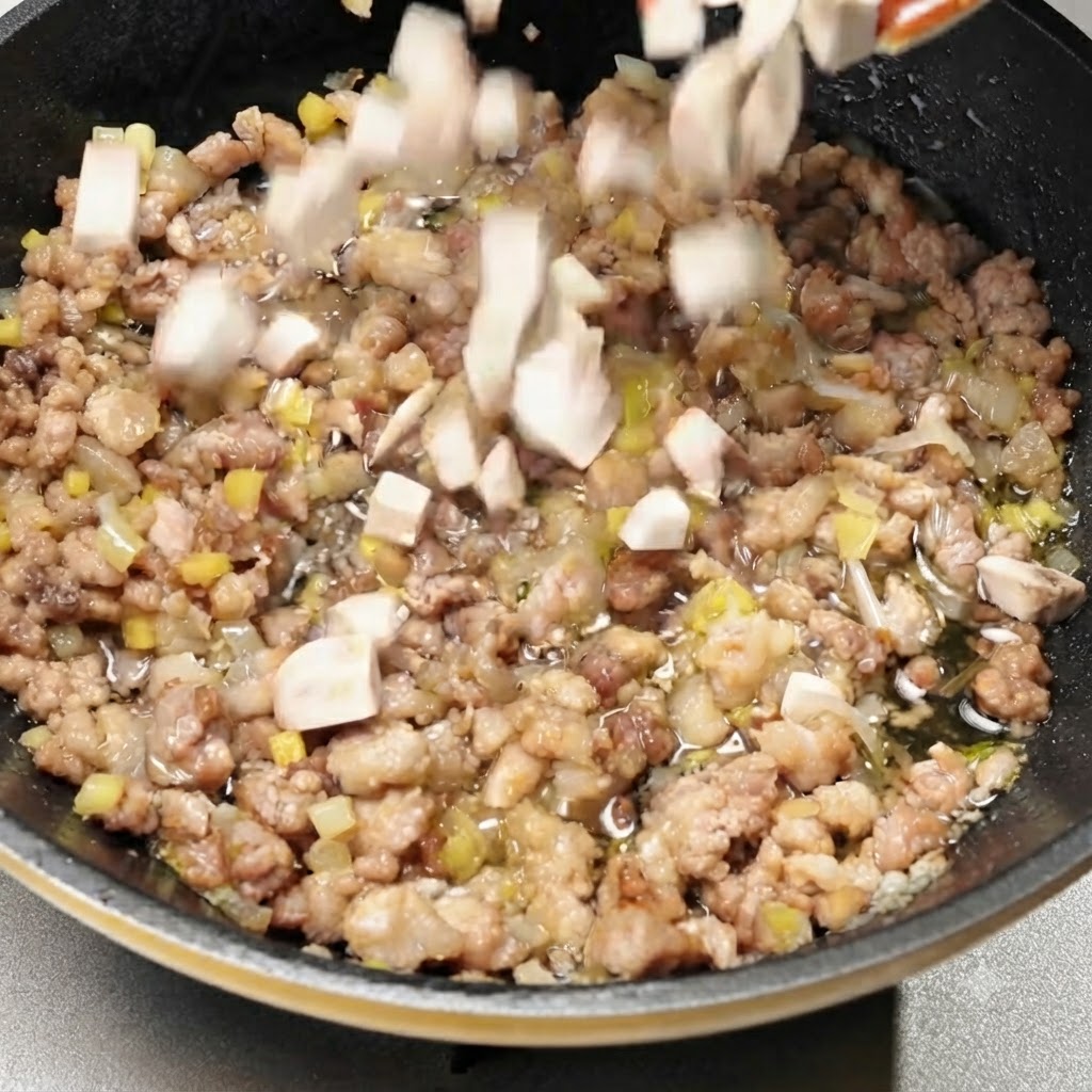 Gewürfelte Champignons werden in die Pfanne mit der gewürzten Schweinefleischmischung gegeben.