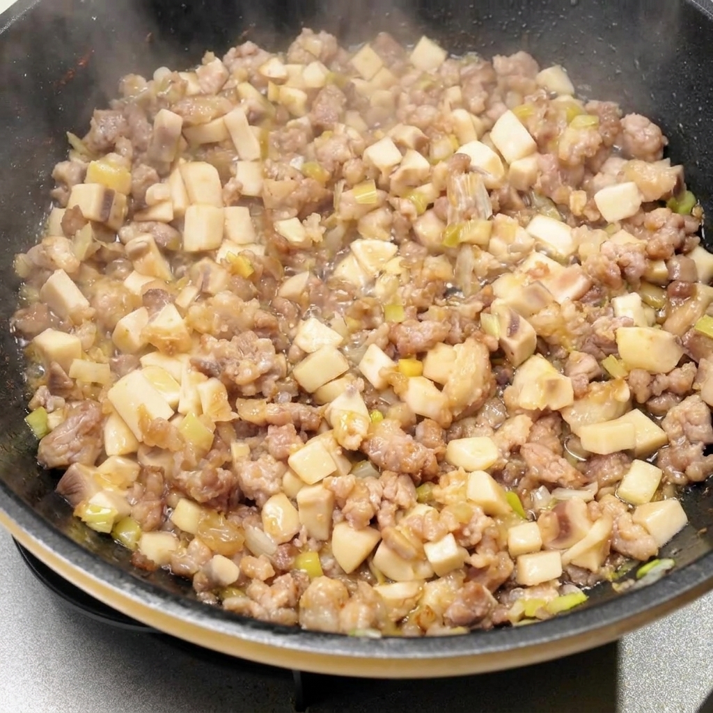 Verschiedene flüssige Gewürze und Saucen werden in die Pfanne mit der Fleisch- und Champignonmischung gegossen.