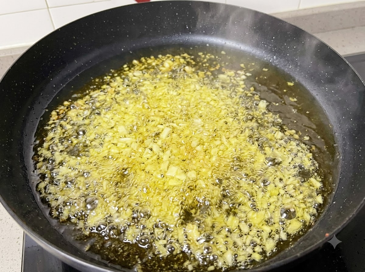 Gehackter Knoblauch und Zwiebeln brutzeln in heißen Öl in einer schwarzen Pfanne.