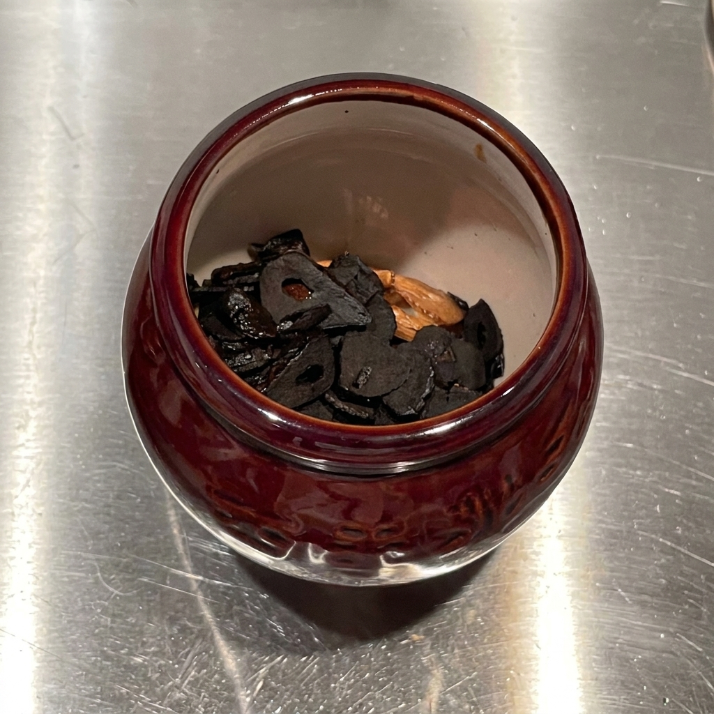 Knoblauchinfundiertes Öl wird von oben in eine mit frittierten Knoblauchchips gefüllte Keramikmörser gegossen.