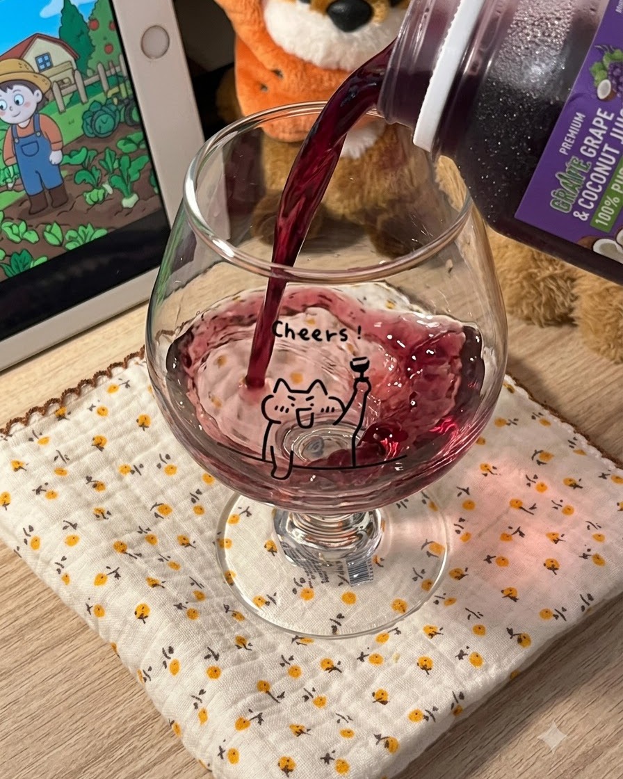 Dunkelviolettes Traubensaftgetränk wird aus einem Karton in ein klares Stielglas mit Cartoon-Katzenmotiv gegossen.