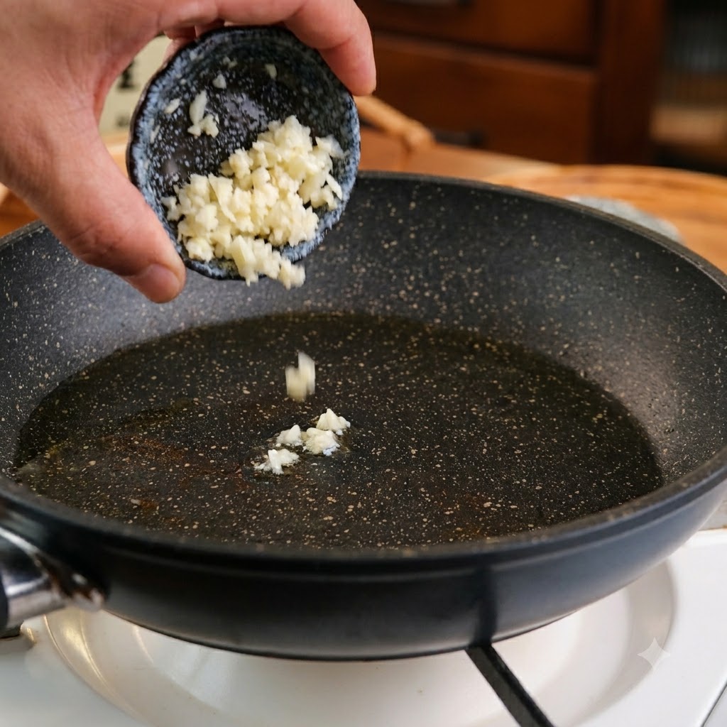 Gehackter Knoblauch wird aus einer kleinen dunklen Schüssel in eine Pfanne mit Öl gegeben.