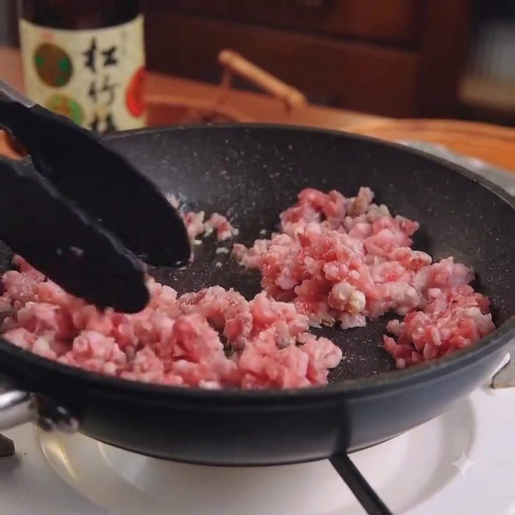 Rohes Schweinehackfleisch und Knoblauch werden mit einer Kochzange in einer schwarzen Pfanne umgerührt.