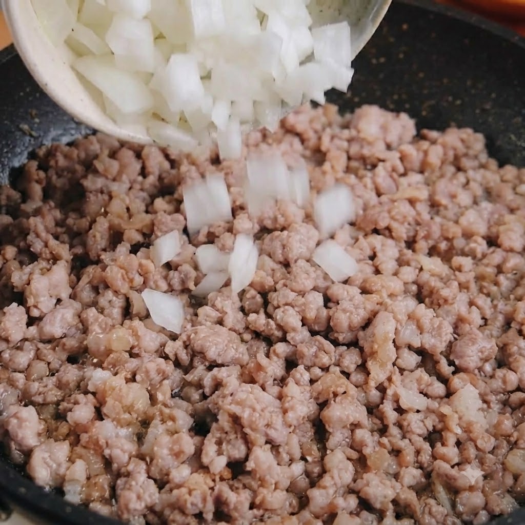 Gewürfelte weiße Zwiebel wird aus einer Schüssel in eine Pfanne mit gekochtem Schweinehackfleisch gegeben.
