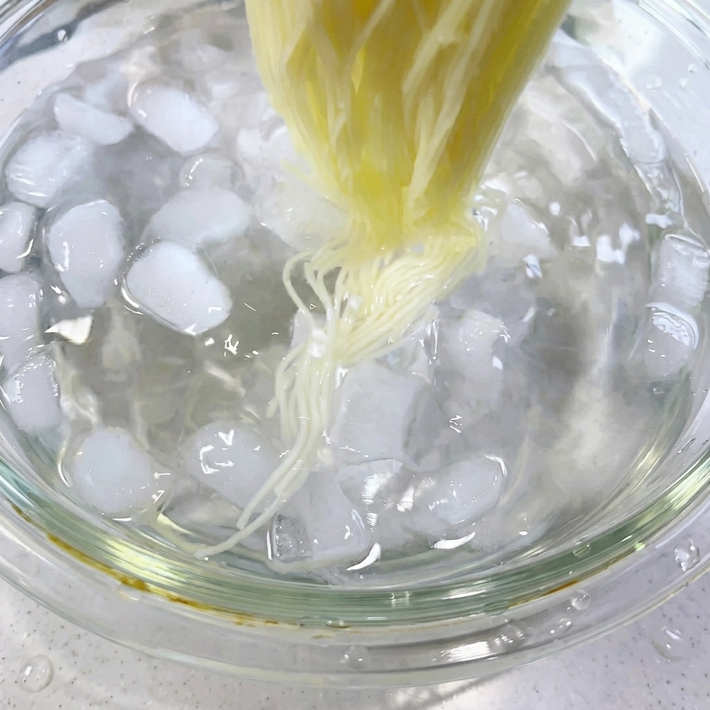 Essstäbchen rühren gekochte Nudeln in einem Eiswasserbad mit Eiswürfeln um.