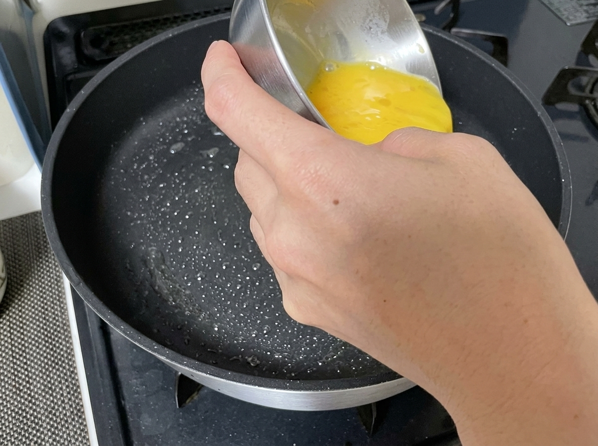 Verquirlte Eierflüssigkeit wird in eine gefettete Bratpfanne gegossen.