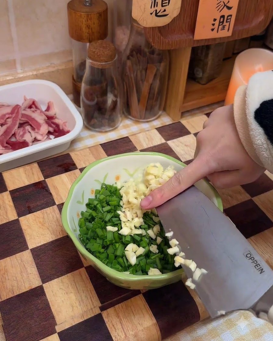 Frisch gehackter Knoblauch wird zu einer Schüssel mit Frühlingszwiebeln und Gewürzen gegeben.