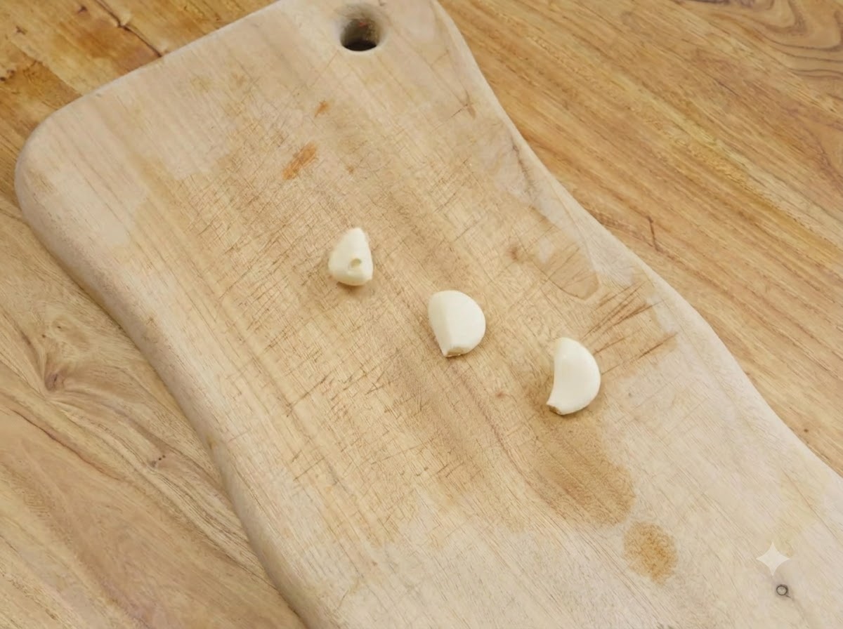 Drei geschälte Knoblauchzehen auf einem Holzschneidebrett.