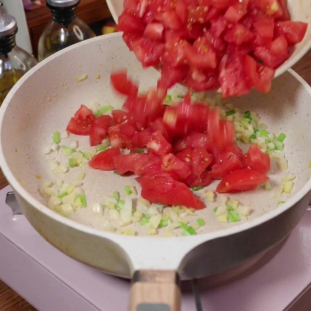 Gewürfelte Tomaten werden in die Pfanne zu den Aromen gegeben.