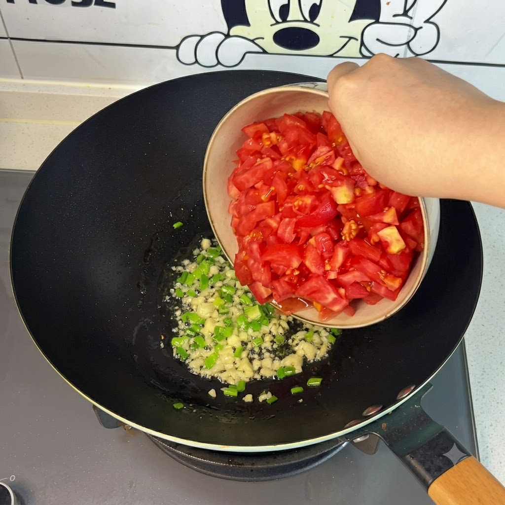 Freshly chopped red tomatoes being poured from a bowl into the wok.