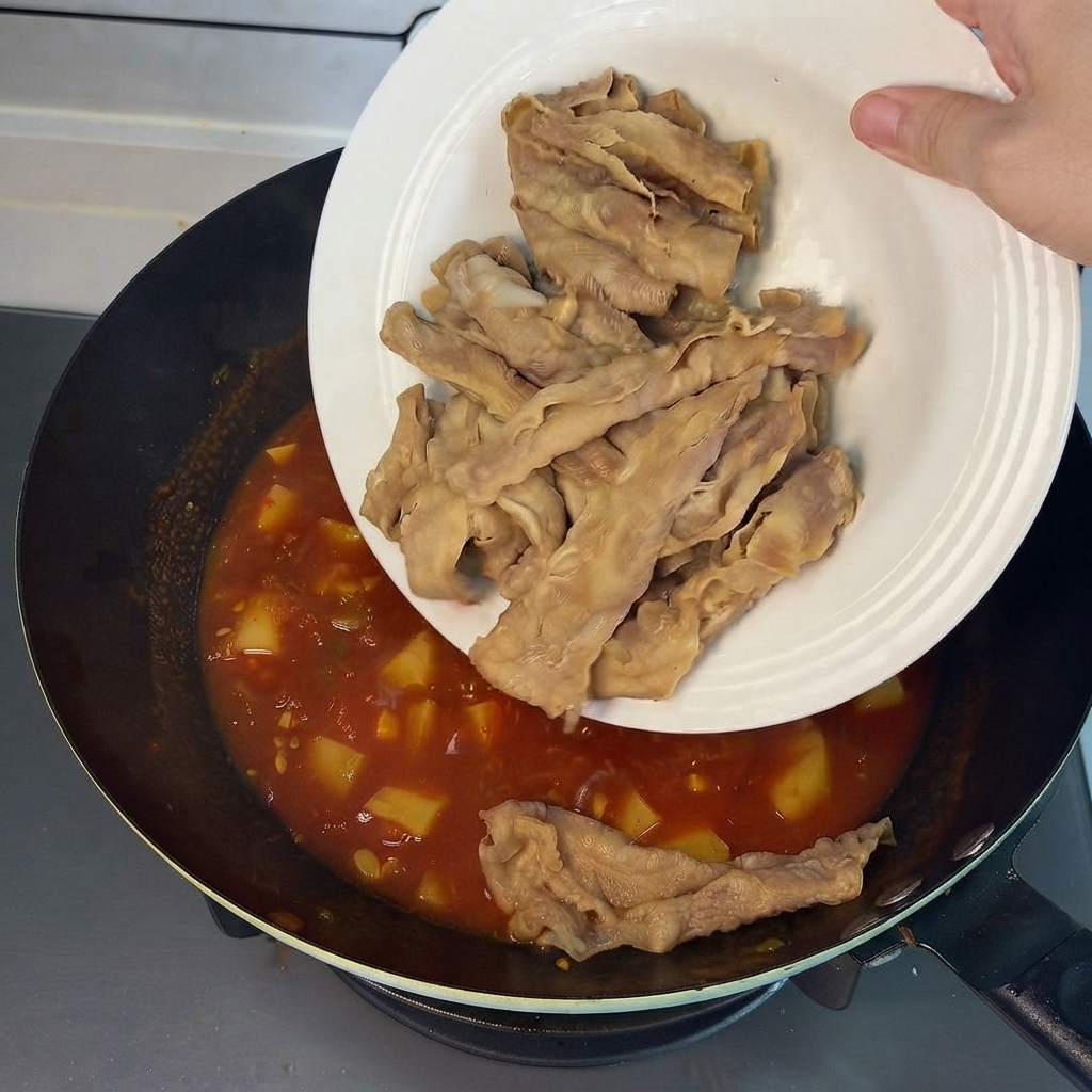 Pre-blanched beef rolls sliding from a white plate into the savory red broth in the wok.