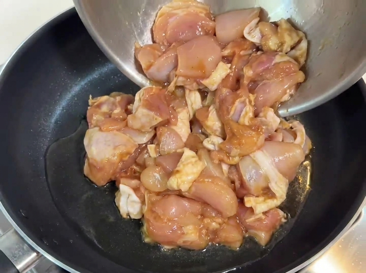 Marinierte Hähnchenstücke werden in eine Pfanne mit heißem Öl gegeben.