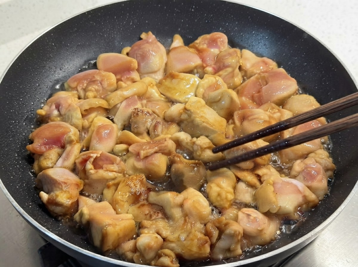 Marinierte Hähnchenstücke braten in einer Pfanne und werden vorsichtig mit Holzstäbchen gewendet.