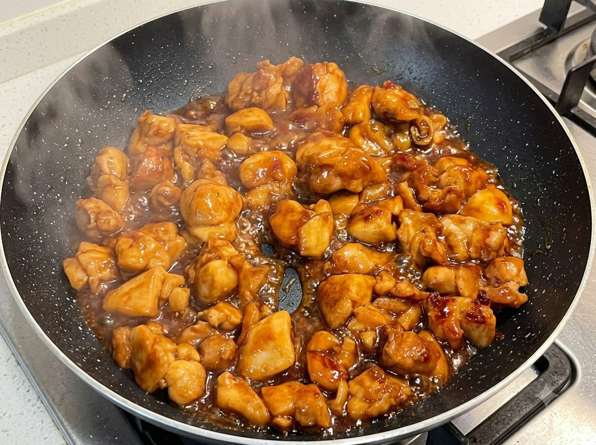 Hähnchen köchelt in einer dicken Sauce in einer Bratpfanne.