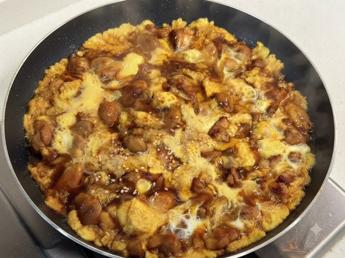 Eine heiße Pfanne mit zart gekochtem Hähnchen und seidigem Ei in einer dunklen Sauce, garniert mit weißem Sesam.