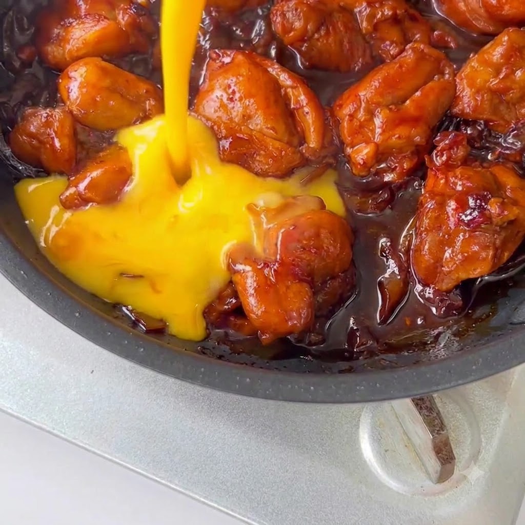 Verquirlte Eier werden in einer Pfanne über Hähnchen und Sauce gegossen.