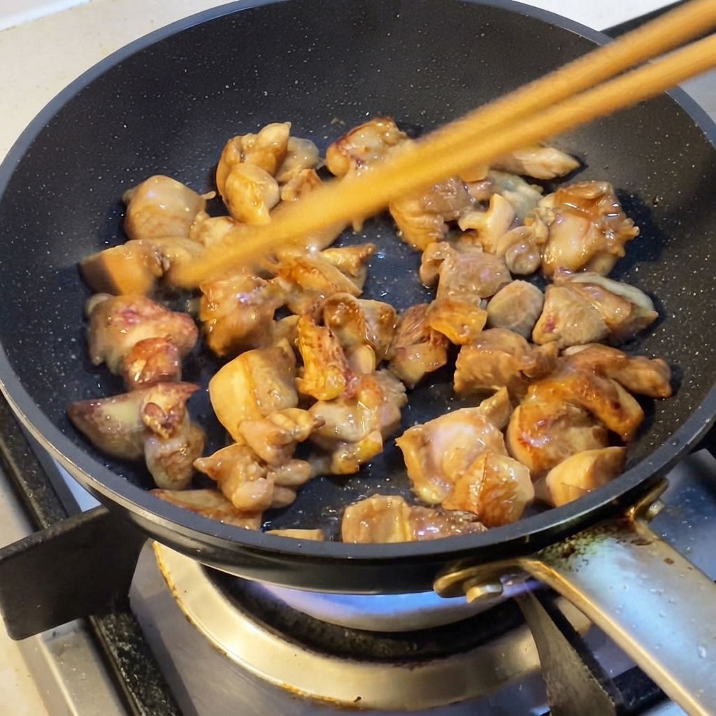 Hähnchenstücke werden mit Essstäbchen in einer Pfanne angebraten.