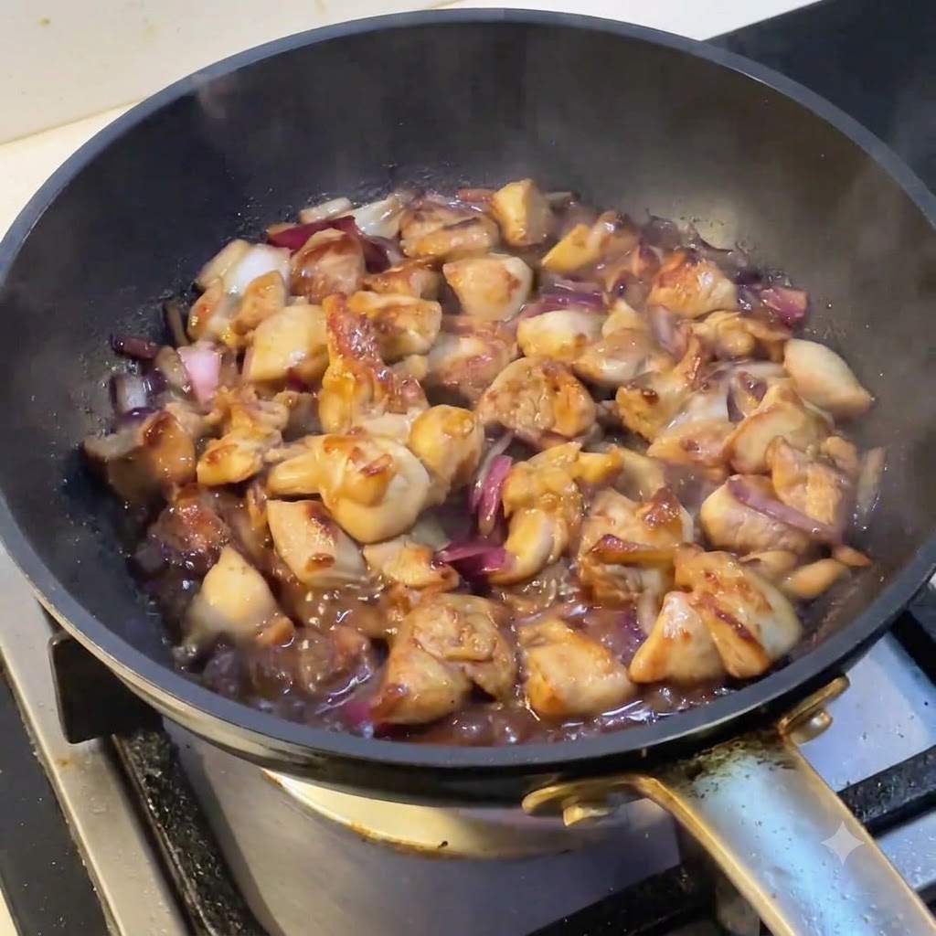 Eine Pfanne mit köchelndem Hähnchen und Zwiebeln, während Dampf von der Oberfläche aufsteigt.
