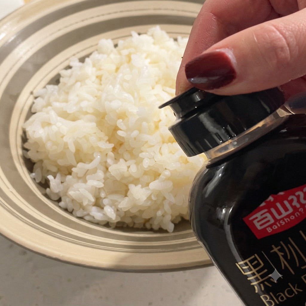 Schwarze Trüffelsoße wird aus einer Flasche auf eine Schüssel mit fluffigem, gedämpftem weißem Reis geträufelt.
