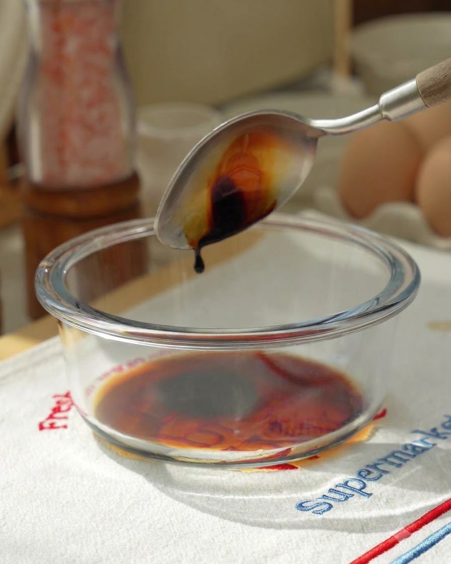 Sojasauce wird von einem Löffel in eine Glasschüssel mit weiteren Saucenzutaten gegossen.