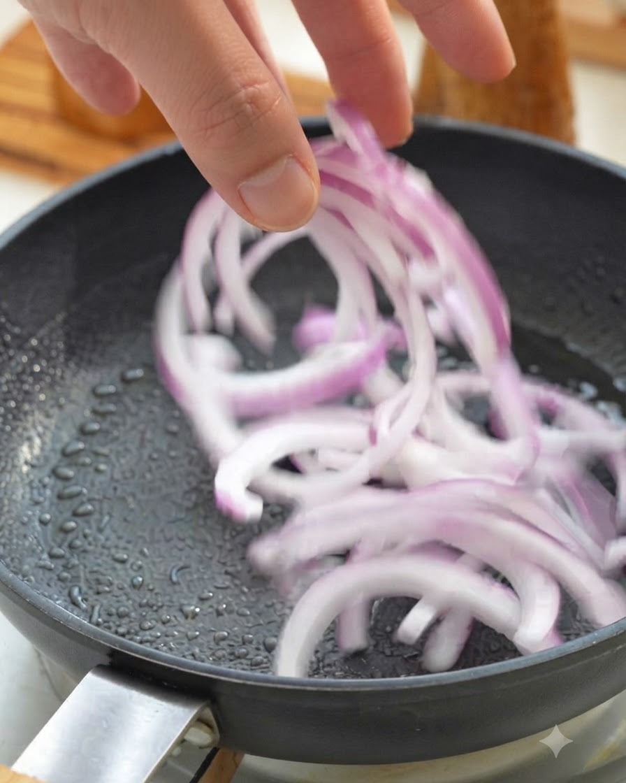 Geschnittene rote Zwiebeln werden in eine heiße Bratpfanne gegeben.
