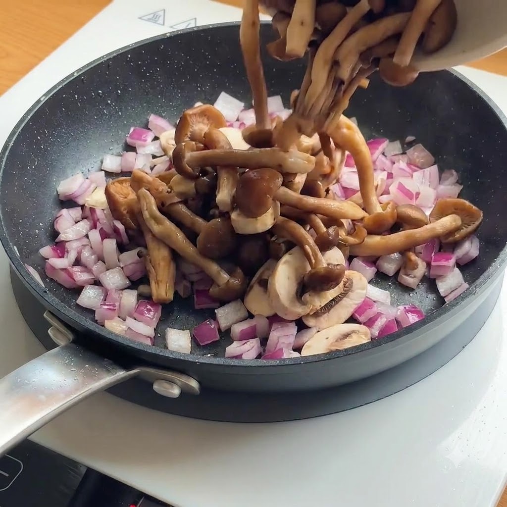 Geschnittene Pilze und rote Zwiebeln werden in eine Pfanne mit bereits angebratenen Hähnchenstücken gegeben.