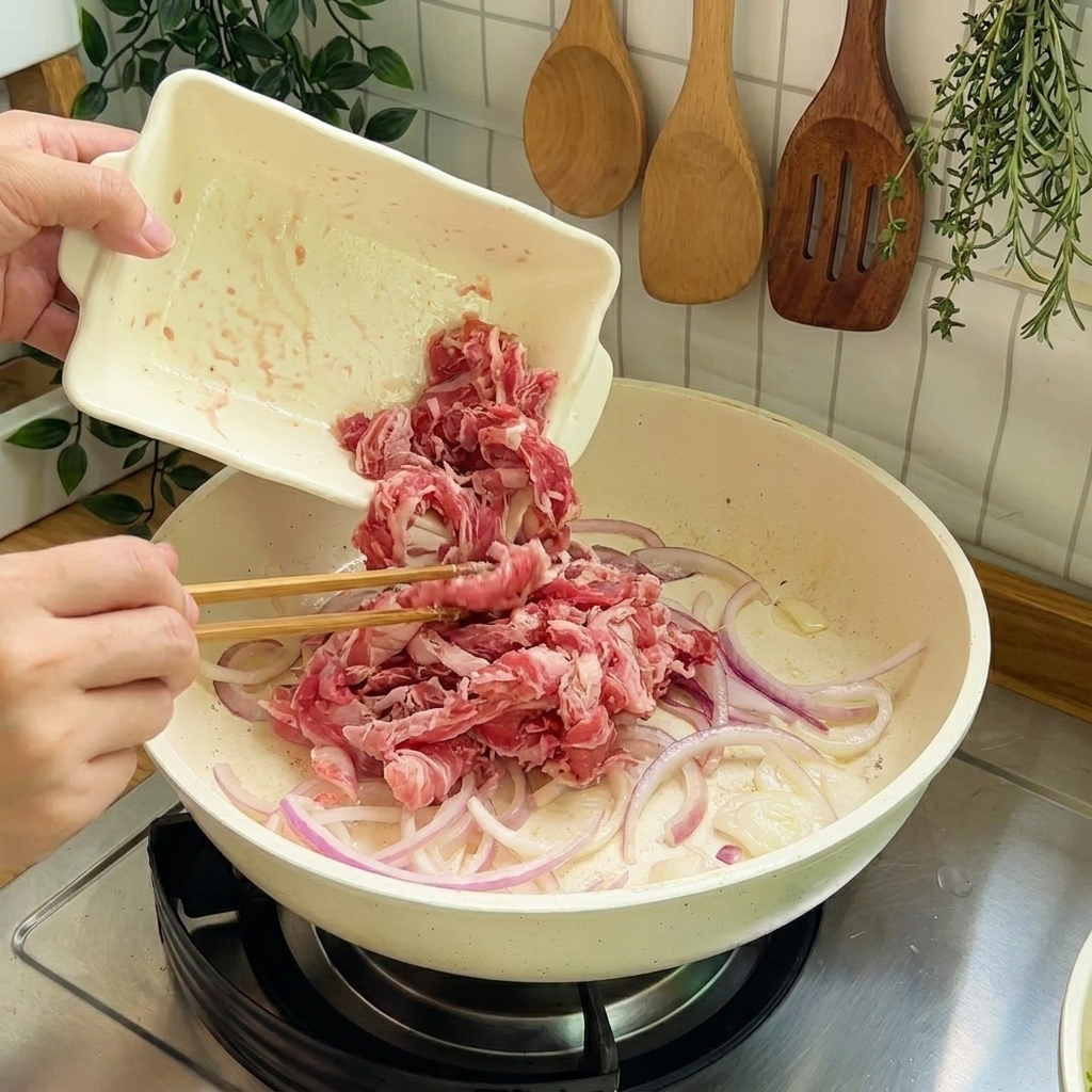 Rohe Rinderstreifen werden zum Anbraten in die Pfanne mit den Zwiebeln gegeben.