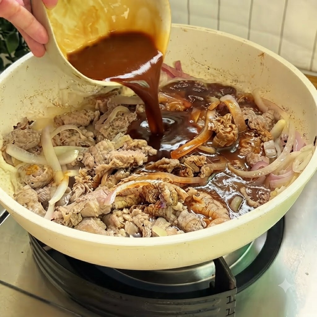 Dunkle Soße wird aus einer kleinen Schüssel in eine weiße Pfanne mit Rindfleisch und Zwiebeln gegossen.