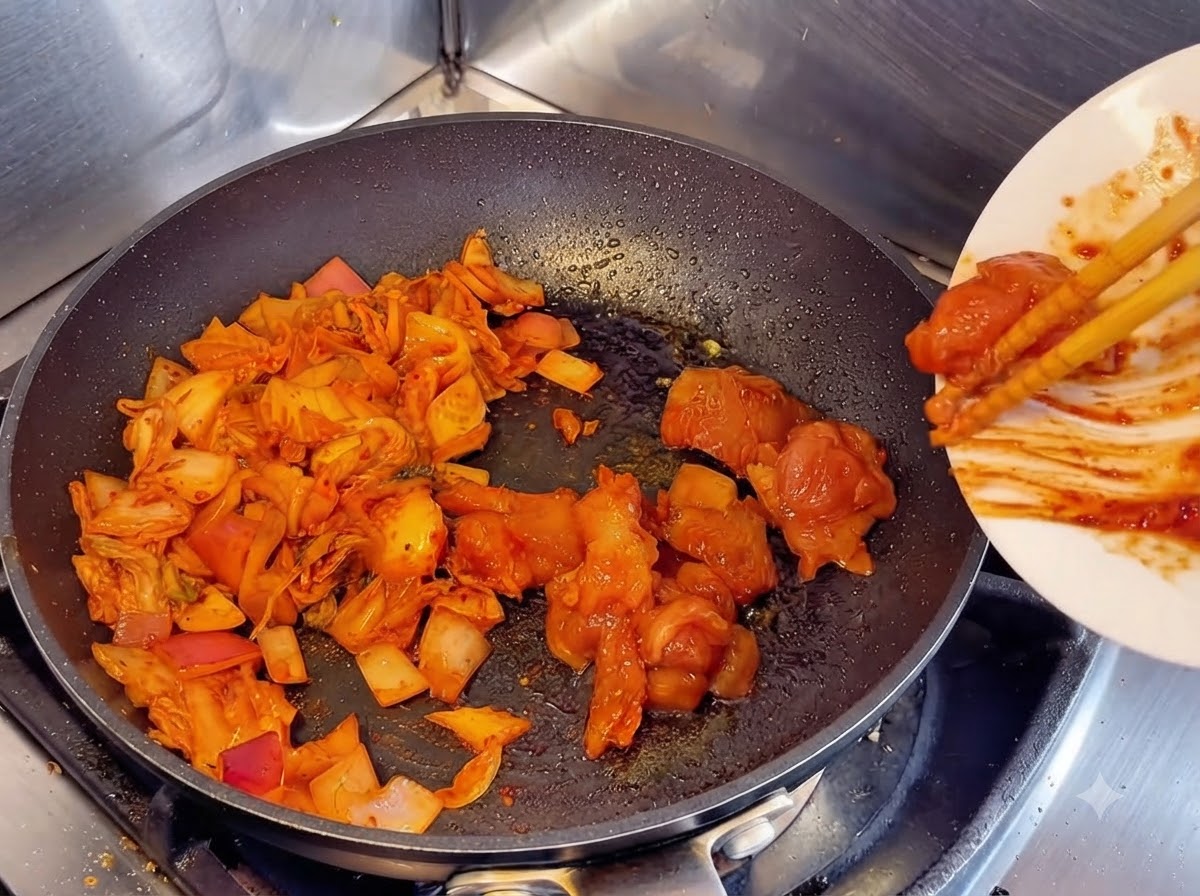 Marinierte rohe Hähnchenstücke werden mit Stäbchen von einem weißen Teller neben angebratenes Kimchi und Zwiebeln in die Pfanne geschoben.