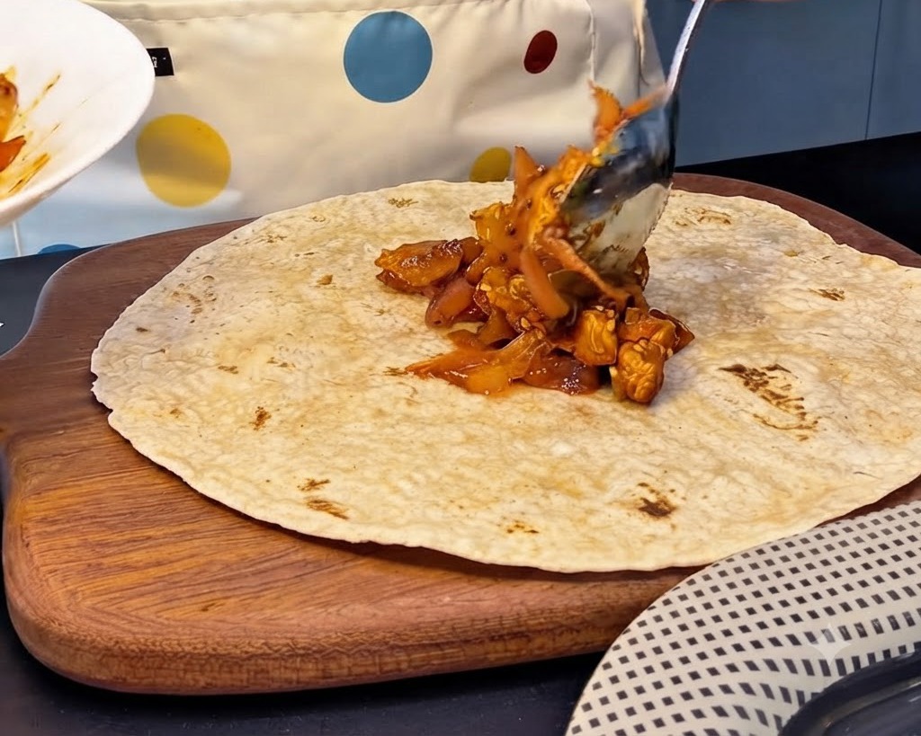 Ein großer Löffel scharfe Hähnchen-Kimchi-Füllung wird in die Mitte einer Vollkorn-Tortilla gegeben.