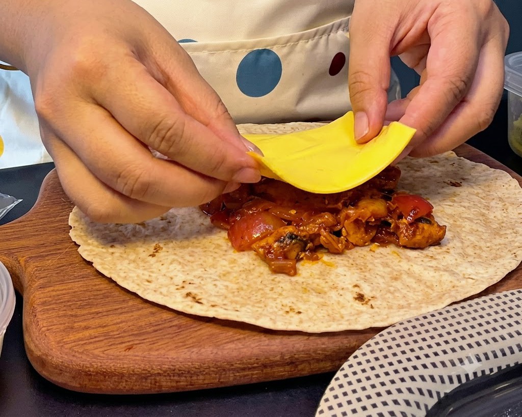 Hände legen eine quadratische Scheibe gelben Käse auf einen Haufen heißer Hähnchen-Kimchi-Füllung auf einem Fladenbrot.