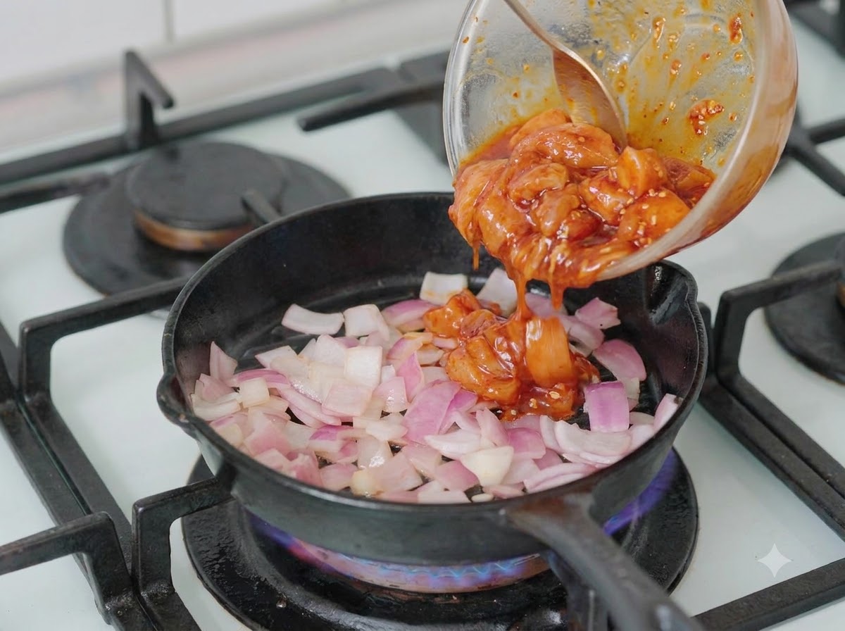 Marinierte Hähnchenstücke werden aus einer Schüssel in eine Pfanne mit gehackten Zwiebeln gegeben.
