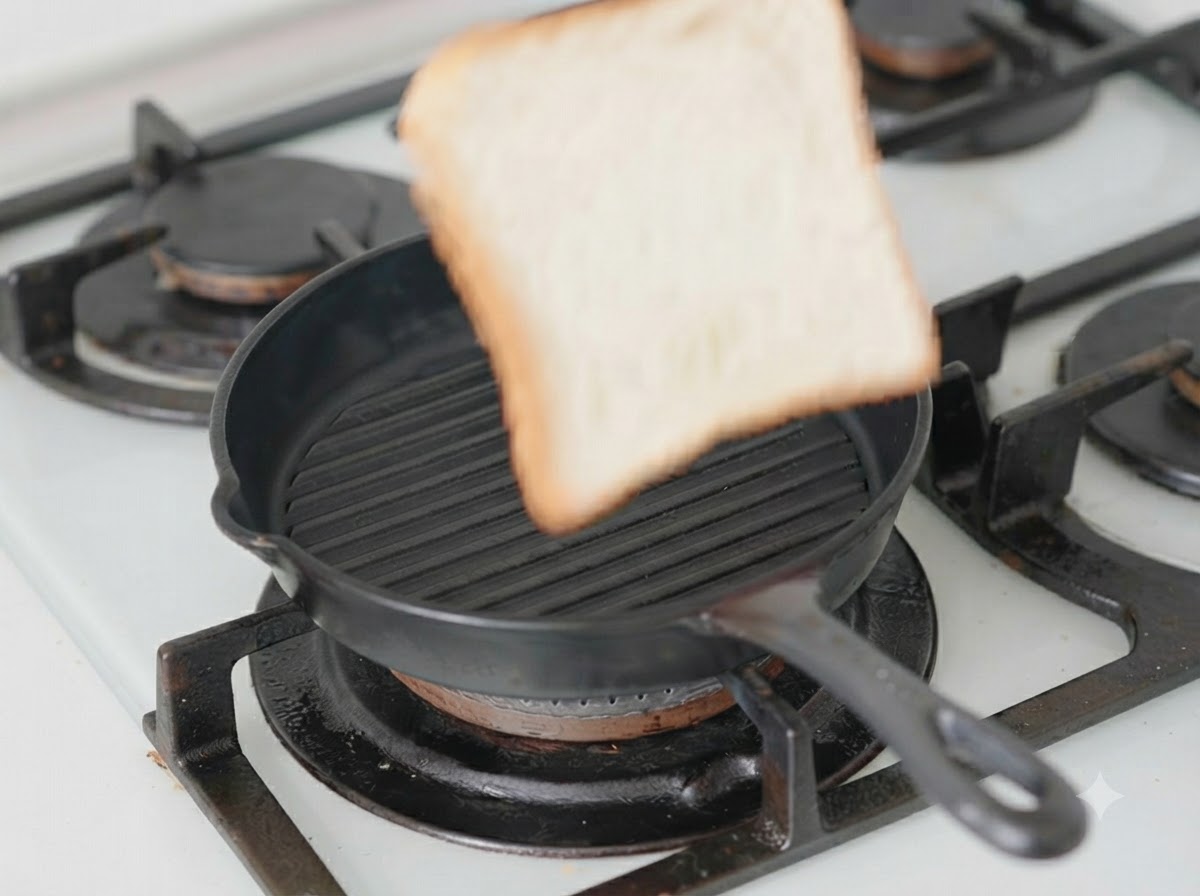 Eine einzelne Brotscheibe liegt in einer schwarzen Grillpfanne mit einer Scheibe Käse darauf.