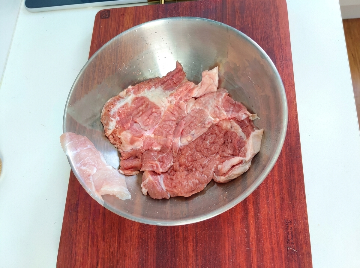 Schweinefleischstücke in einer Metallschüssel mit Marinadezutaten.