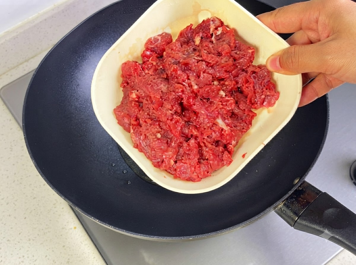 Rinderhackfleisch wird zum Anbraten in eine heiße Pfanne mit Öl gegeben.
