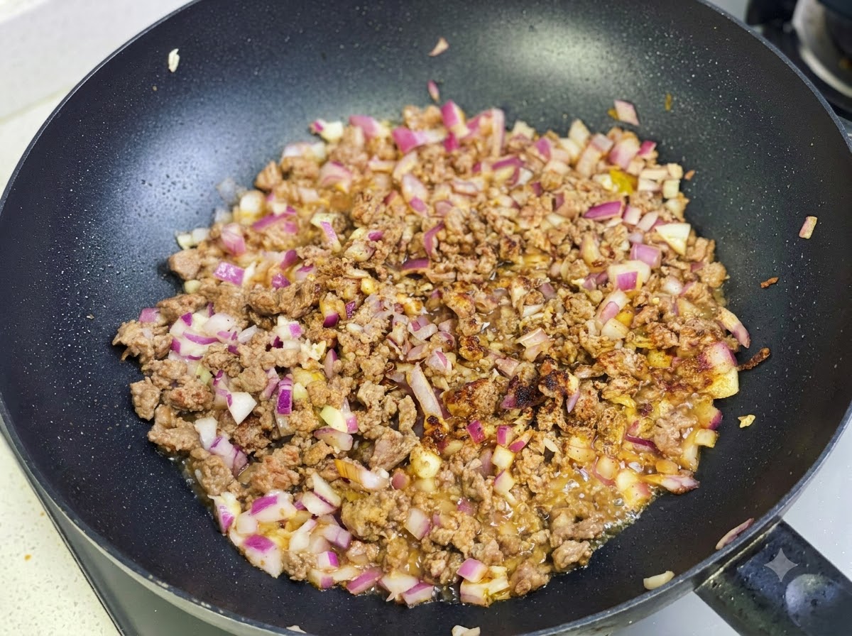 Currypaste und Gewürze werden mit der Rindfleisch-Zwiebel-Mischung in der Pfanne angebraten.