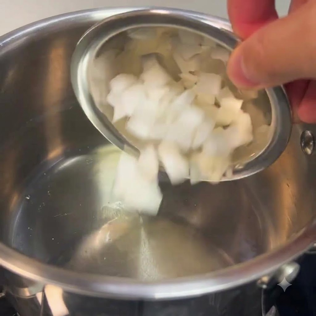 Gehackte weiße Zwiebeln werden aus einer kleinen Schüssel in einen Edelstahltopf gegeben.