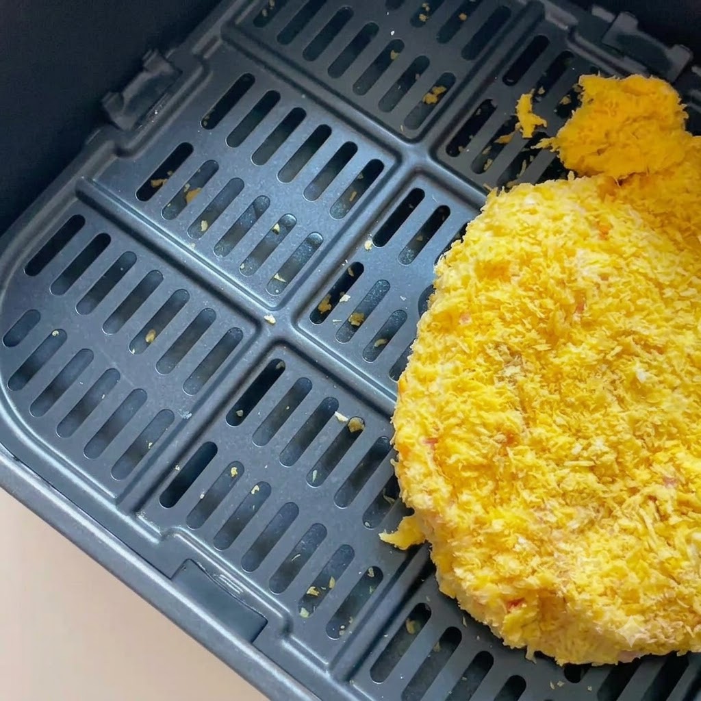 Ein paniertes Schweineschnitzel in einem dunklen Korb der Heißluftfritteuse.