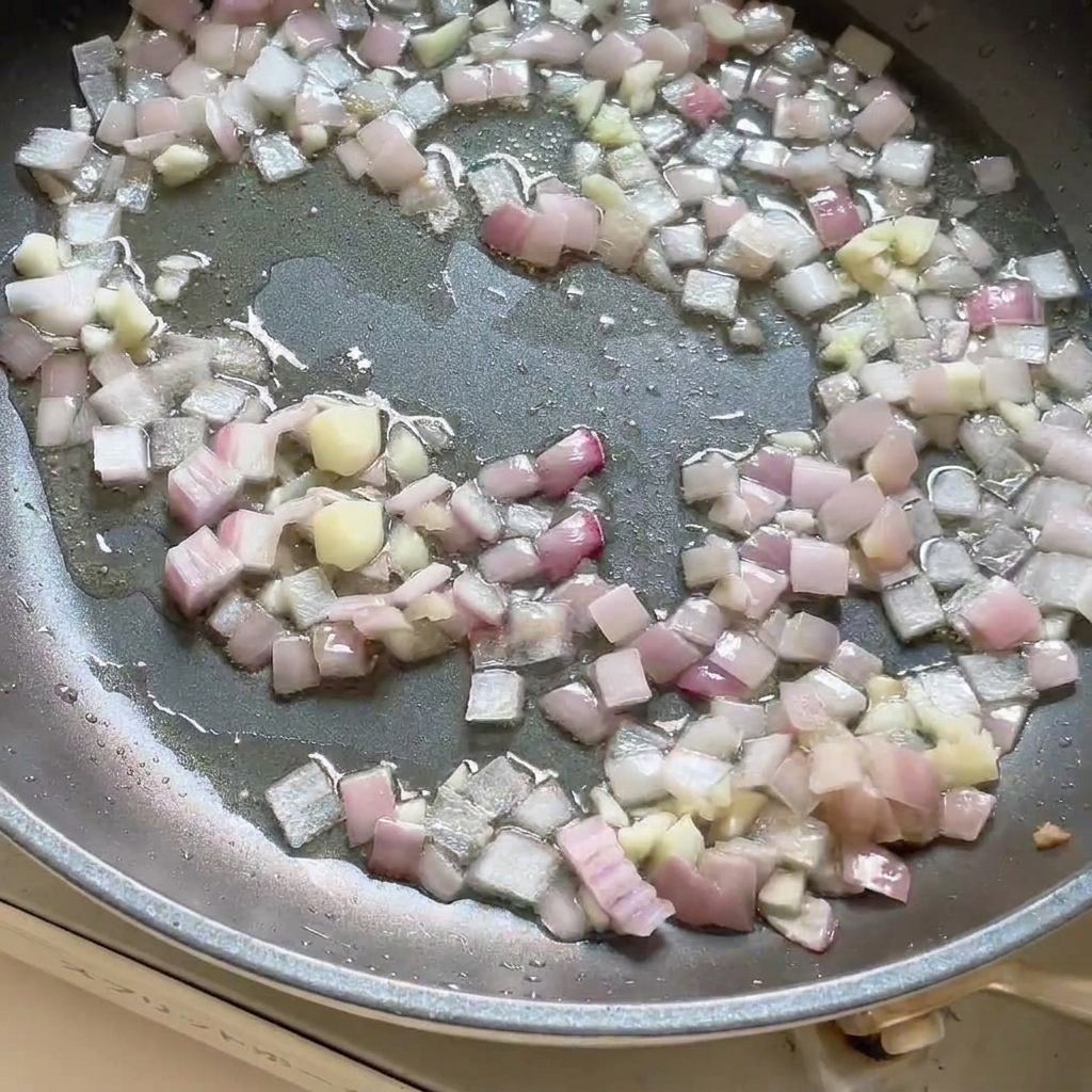 Currypaste wird in die Pfanne mit den angebratenen Zwiebeln und Knoblauch gegeben und verrührt.