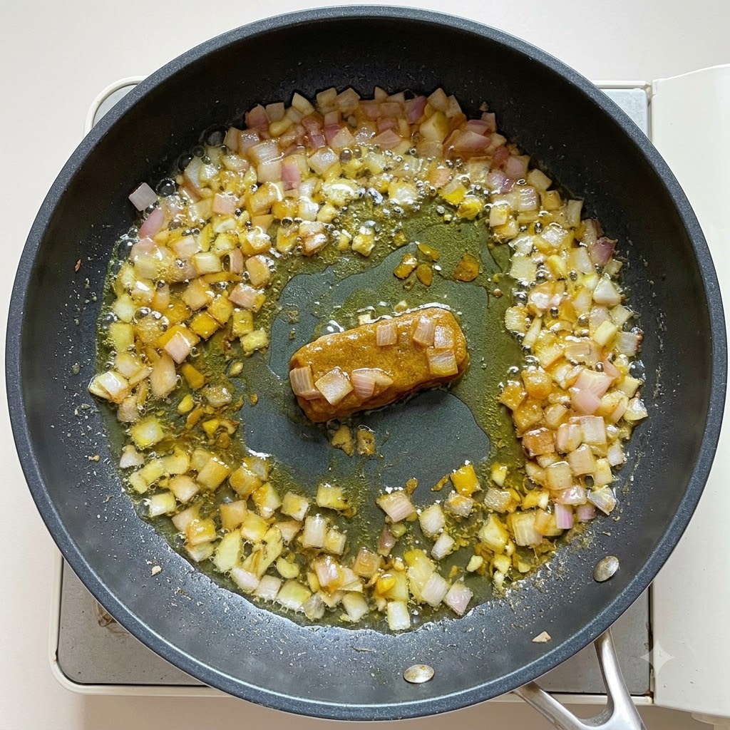 Wasser und Kokosmilch werden in die Currybasis in der Bratpfanne gegossen und zu einer dicken Konsistenz verrührt.
