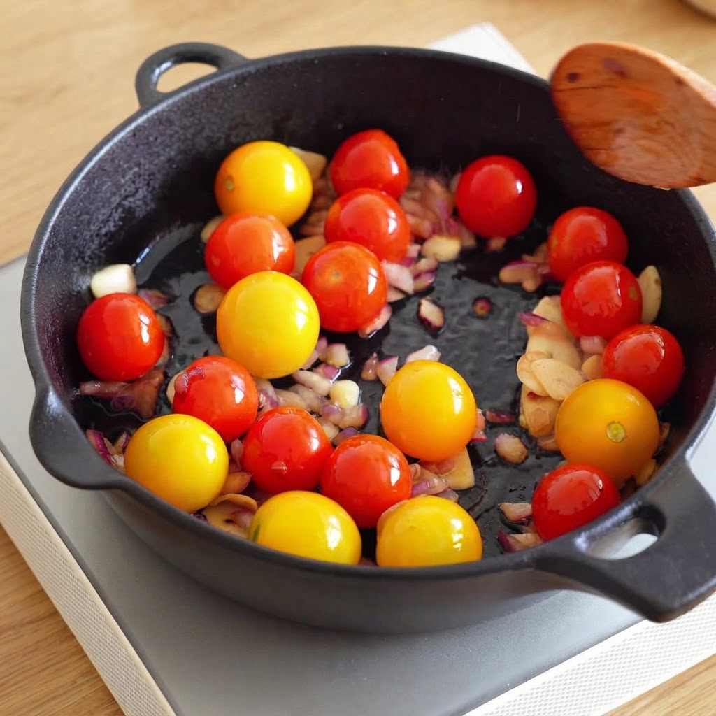 Ein Holzlöffel wird über eine Pfanne mit Kirschtomaten, gehackten Zwiebeln und Knoblauch gehalten.