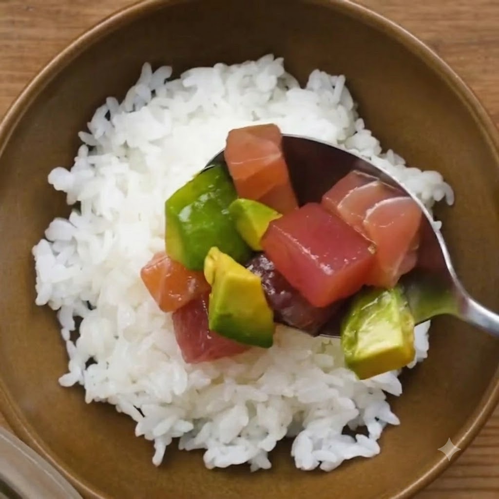 Ein Löffel marinierter Thunfisch und Avocado wird auf eine Schüssel mit weißem Sushi-Reis gegeben.