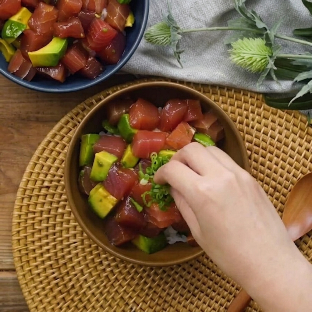 Eine Hand streut gehackte Frühlingszwiebeln über die Thunfisch-Avocado-Schüssel.