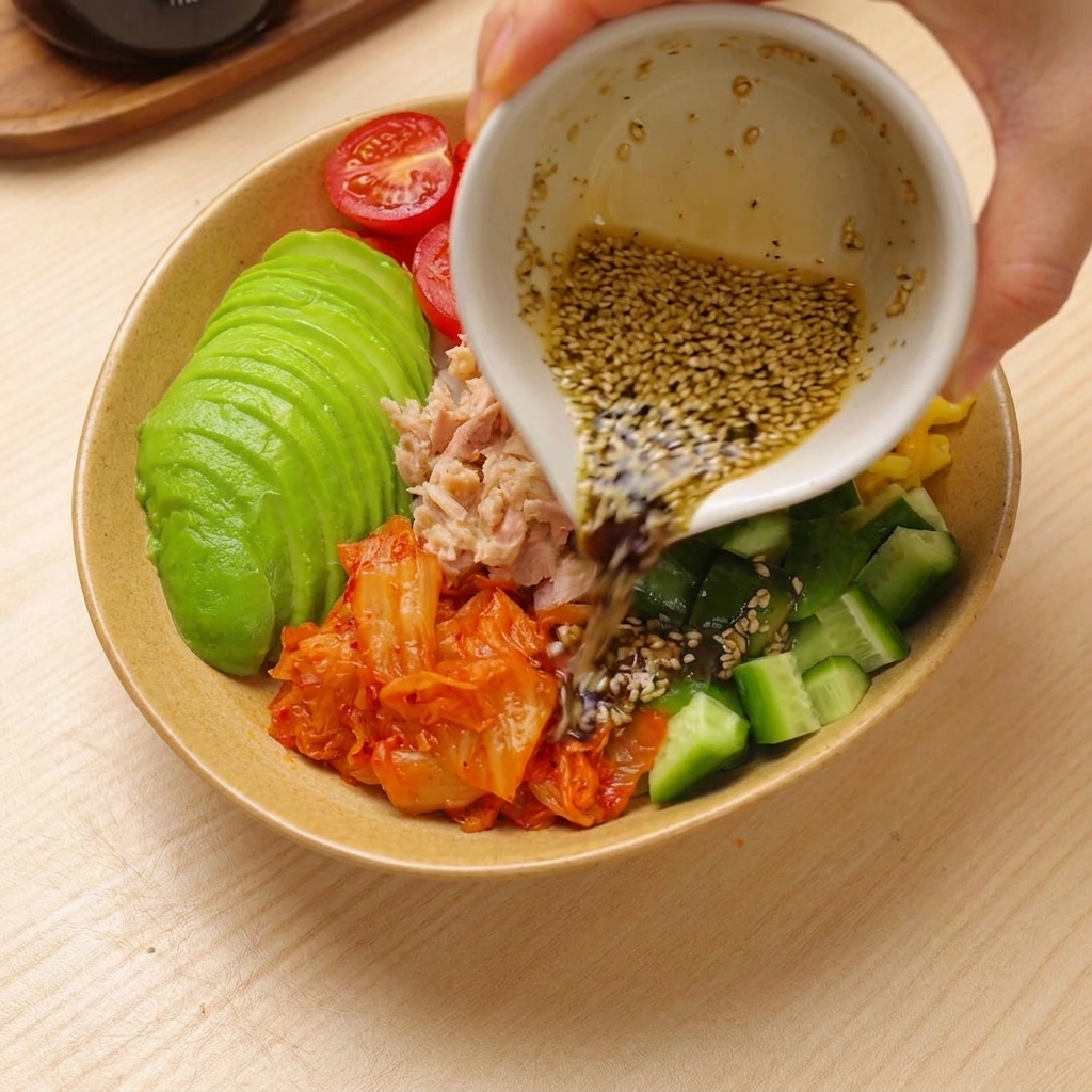 Dressing wird über eine bunt zusammengestellte Thunfisch-Avocado-Reis-Bowl gegossen.