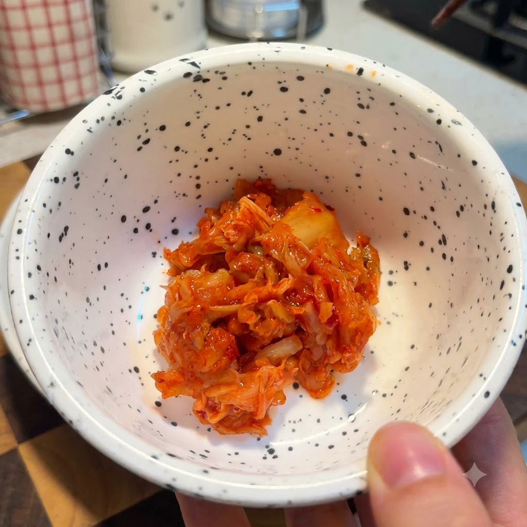 Eine weiss gesprenkelte Schüssel gefüllt mit einer Portion hellrotem, gehacktem Kimchi.