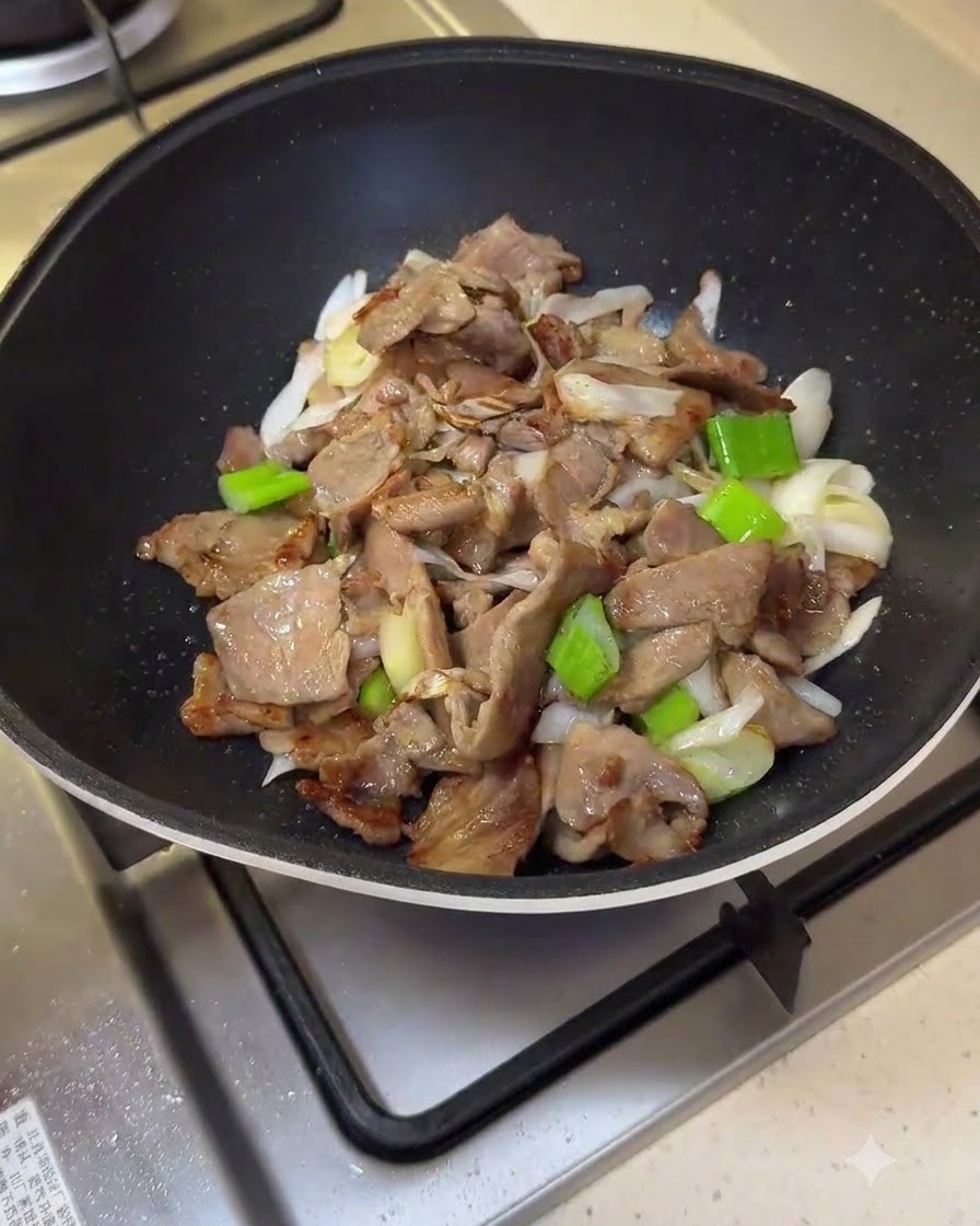 Die rote Saucenmischung wird über das Schweinefleisch und die Frühlingszwiebeln in die Bratpfanne gegossen.