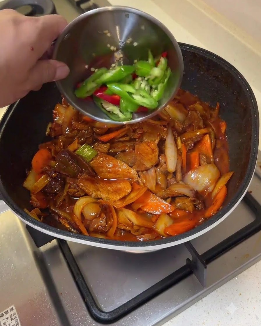 Grüne und rote Chilischotenscheiben werden aus einer kleinen Schüssel in eine Pfanne mit angebratenem Schweinefleisch und Gemüse gegeben.